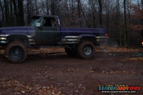 Purple lifted pickup truck with off-road tires parked on a dirt path in a wooded area