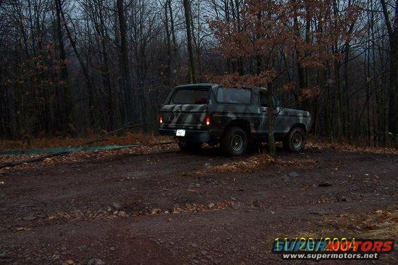 Camouflaged Ford Bronco parked on a dirt road in a forest