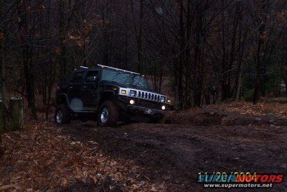 Black Hummer H2 driving off-road through mud and trees