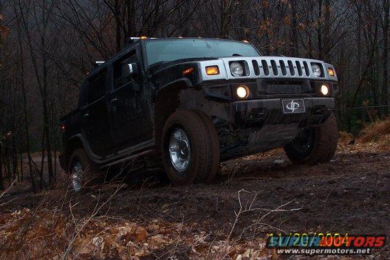 Black Hummer H2 with chrome grille driving through muddy terrain, trees in background. Watermark reads 11/20/2004