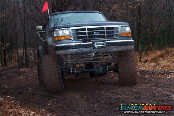 Dark blue Ford truck with large tires on a muddy trail