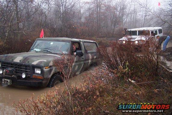 Camouflaged 1979 Ford Bronco stuck in mud, 3q-front view