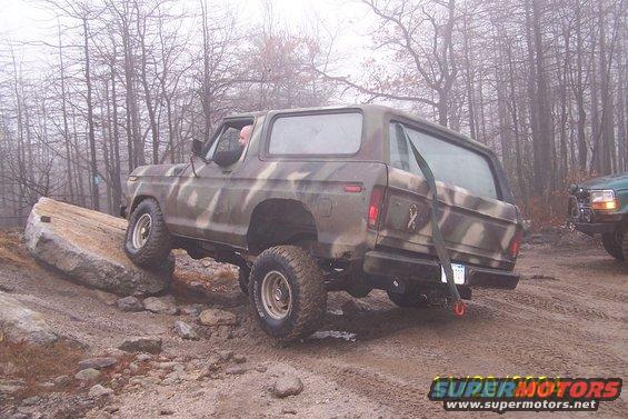 Camouflaged Ford Bronco climbing over a rock on a dirt trail