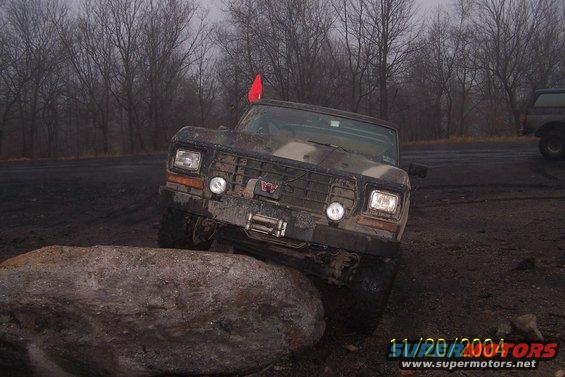 1979 Ford Bronco with camouflage paint, front view, off-roading over a rock