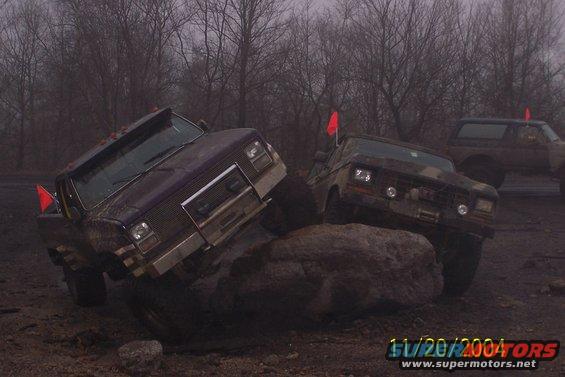 Purple and camouflage off-road trucks climbing over rocks on a muddy course