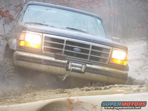 1995 Ford Bronco driving through mud, front view with headlights on