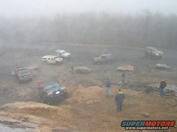 multiple off-road vehicles driving on a muddy terrain with fog in the background