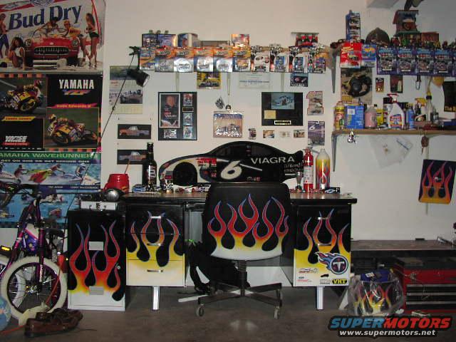 Garage interior with shelves of collectibles, a desk with flame decals, and a racing car graphic on the wall