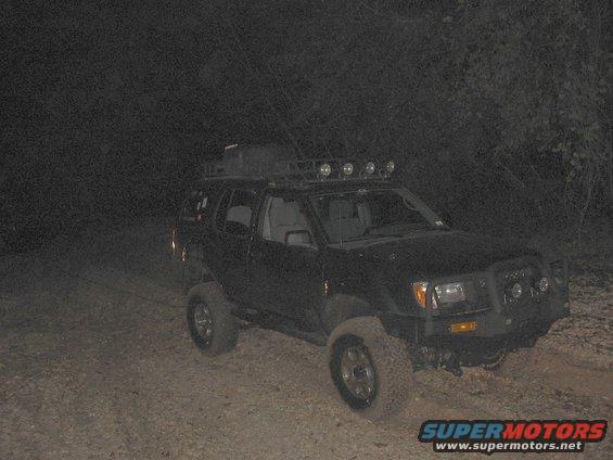 Black SUV with roof rack and off-road lights parked on dirt road at night