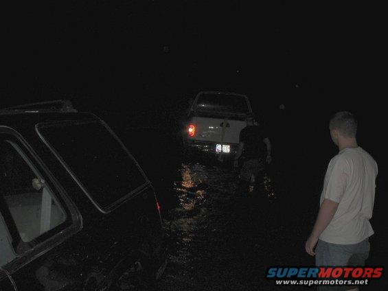 Two trucks partially submerged in water at night, with a person standing nearby