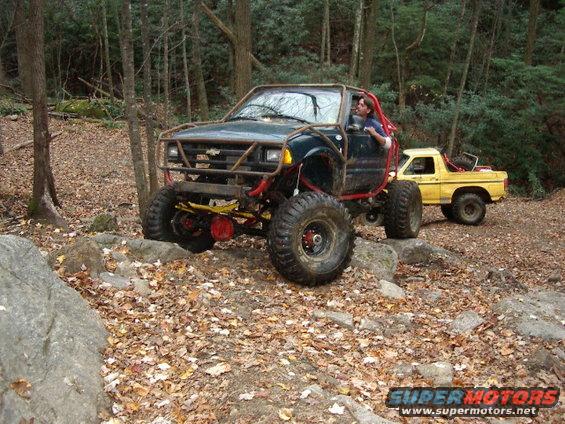 Modified dark green SUV with roll cage and large tires, yellow pickup truck behind