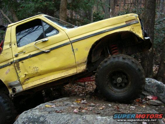 Yellow off-road truck with large tires and lifted suspension, angled on rocks