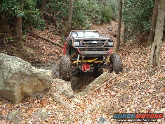 Off-road vehicle with custom roll cage navigating a muddy, rocky trail