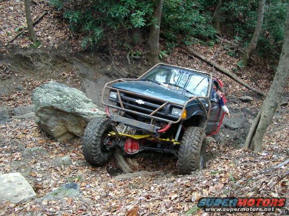 Off-road vehicle with roll cage climbing over rocks and logs on a wooded trail