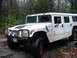 1979 Ford Bronco - A white Hummer H1 sits on a muddy dirt road, its windshield cracked, surrounded by trees.