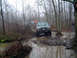 1979 Ford Bronco - Multiple SUVs traverse a wet and muddy path through a dense forest on an overcast day.