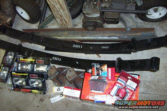 Leaf springs, auxiliary light kits, air filter, and ignition parts laid out on a concrete floor