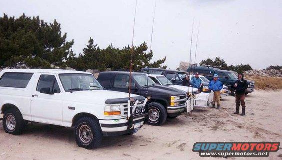 White Ford Bronco parked on a sandy beach with fishing rods