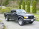 2003 Ford Ranger - A black 2003 Ford Ranger pickup truck is parked outdoors with a wooded area and fence in the background.