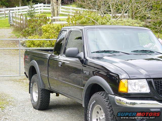 Black 2003 Ford Ranger pickup truck parked on gravel near a white fence