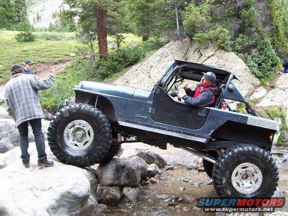 Dark blue Jeep Wrangler navigating rocky terrain, driver giving a thumbs up