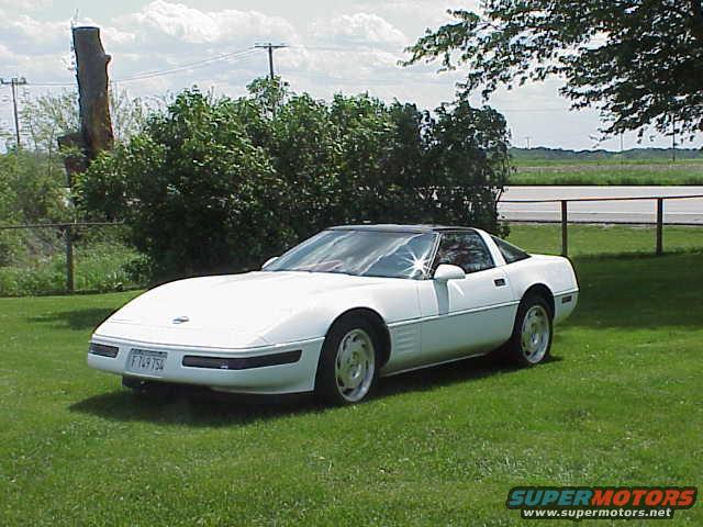 White 1994 Chevrolet Corvette parked on grass with a tree and bushes in the background