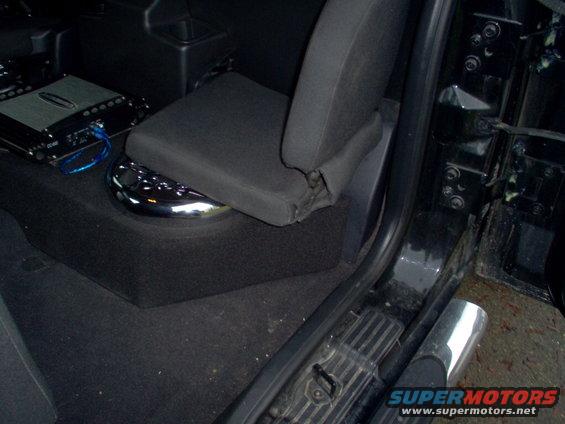 Black interior of a vehicle showing a car seat, amplifier, and chrome cup holder