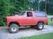 1981 Ford Bronco - This red Ford Bronco SUV is parked on a concrete driveway with grass and trees in the background.