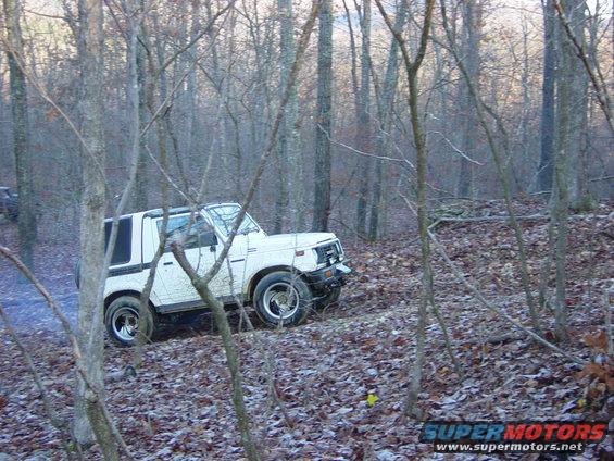 White Suzuki Samurai driving on a wooded trail with fallen leaves