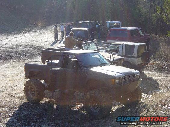 Several modified off-road vehicles parked on a dirt path with trees in the background