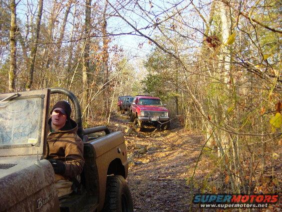 Tan 1974 Ford Bronco driving on a rocky trail with other vehicles behind