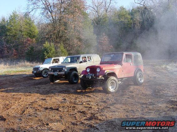 Three off-road vehicles parked on a dirt track with trees in the background