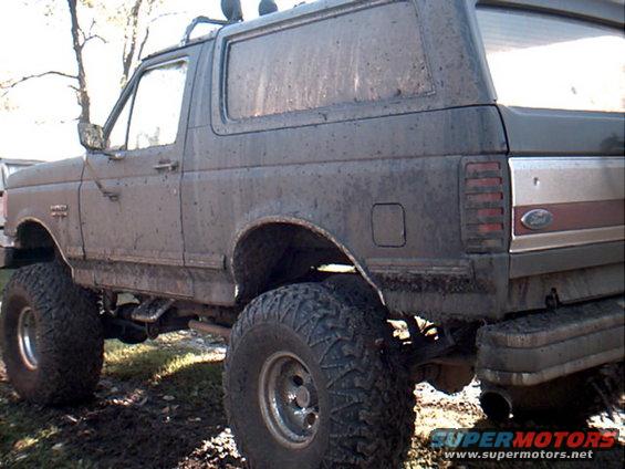 Mud-covered 1990 Ford Bronco, lifted with large tires, parked in dirt