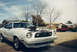 1976 Ford Mustang II - White 1976 Ford Mustang II with hood open, parked in a driveway with a red pickup truck behind it.
