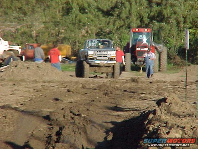 1987 Ford Ranger pickup truck parked in mud with a red tractor behind it