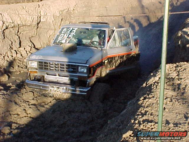 1987 Ford Ranger truck stuck in mud, front view, chrome bumper, orange and black stripe on door