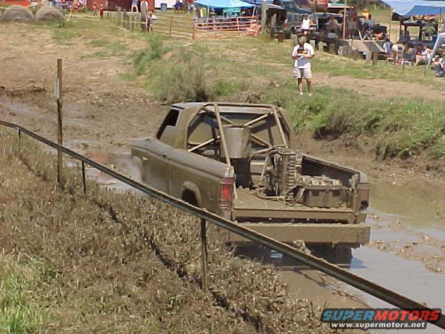 muddy pickup truck with roll cage driving through a mud pit