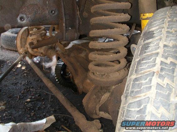 Close-up of rusty front axle, coil spring, and tire from a vehicle