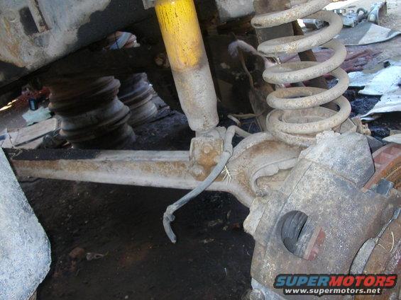 Close-up of a vehicle's front axle, showing the shock absorber, coil spring, and brake caliper