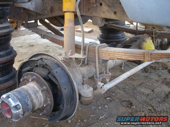 Front axle assembly with drum brakes and leaf springs, showing rust and wear