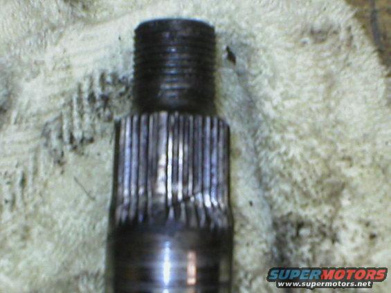 Close-up of a damaged metal shaft with splines and threaded end, resting on a textured cloth
