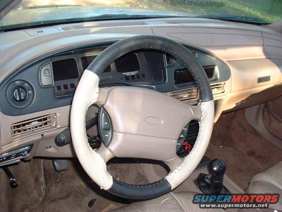 Car interior shot showing steering wheel, dashboard, and gear shift. Steering wheel has a two-tone cover