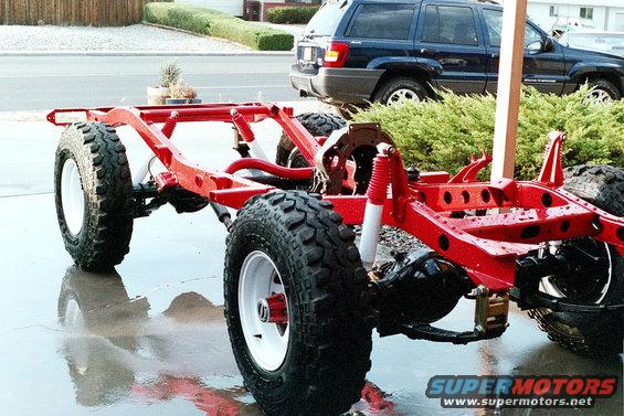 Red vehicle frame with large tires, blue SUV in background