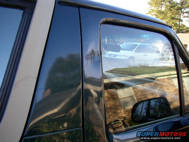 Dark green 1995 Ford Bronco side view, showing reflection of a white minivan and a brick house