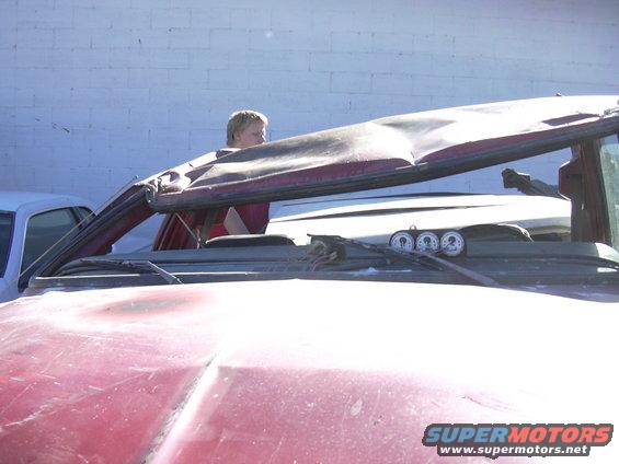 Person looking out of a red SUV with a dented roof. Three gauges are visible on the dashboard
