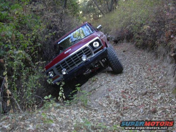Red 1978 Ford Bronco navigating a steep, rocky trail with trees on the left