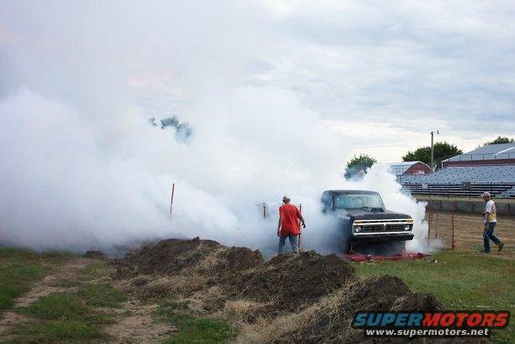 Black pickup truck emitting smoke, front view, with people nearby
