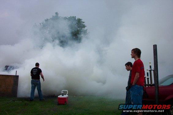 People watch as a large cloud of smoke billows from a structure on the left