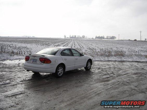 1999 Oldsmobile Alero parked on a muddy road with a snowy field behind it