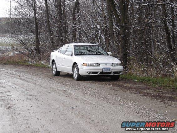 White 1999 Oldsmobile Alero sedan on a dirt road in winter